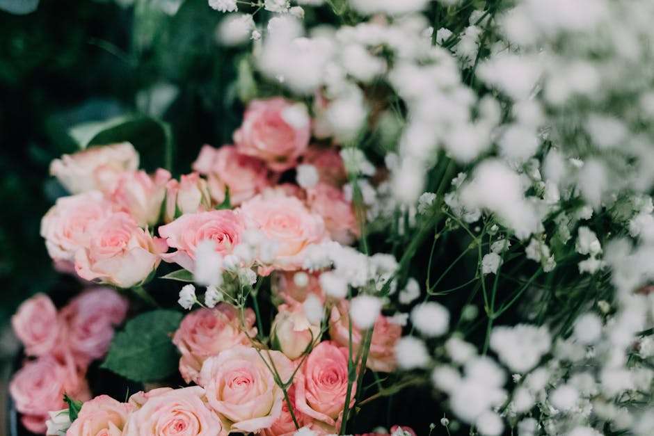 A close-up view of a floral arrangement featuring light pink roses with tightly packed petals, complemented by delicate white baby's breath flowers with tiny clustered blooms and slender stems. The ro
