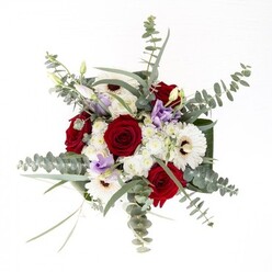 As a seasoned florist in Becontree Heath, I recognize in this striking bouquet the subtle artistry born from experience and a genuine love of the craft. The composition begins with robust red roses, their rich color and velvety touch evoking enduring affection-much like the steadfast bonds that knit together Becontree Heath's residential streets. Creamy white gerbera daisies anchor the ensemble, their rays shining out from bold brown centres, offering brightness that feels both timeless and contemporary. Nestled amid them are lisianthus flowers in pale lavender and lilac, their petals so soft they appear almost translucent in the shifting daylight that filters through the shop windows near Valence Park. Whisper-fine clusters of delicate white filler add gentle elevation and softness, allowing the arrangement to feel airier and more personable. Silver-green eucalyptus leaves weave their refreshingly crisp texture and architectural grace throughout, a breath of nearby woodland on a summer stroll. At the foundation, beautifully wrapped structural foliage frames the bouquet, each shiny, deep green leaf amplifying the vitality of the florals above. Visible through the clear vase, fresh stems extend into pristine water, completing a look of effortless refinement. Perfect for expressing gratitude, celebrating milestones, or simply sending cheer, this bouquet speaks to the heart of the Becontree Heath community, where heartfelt connections and attention to detail flourish.